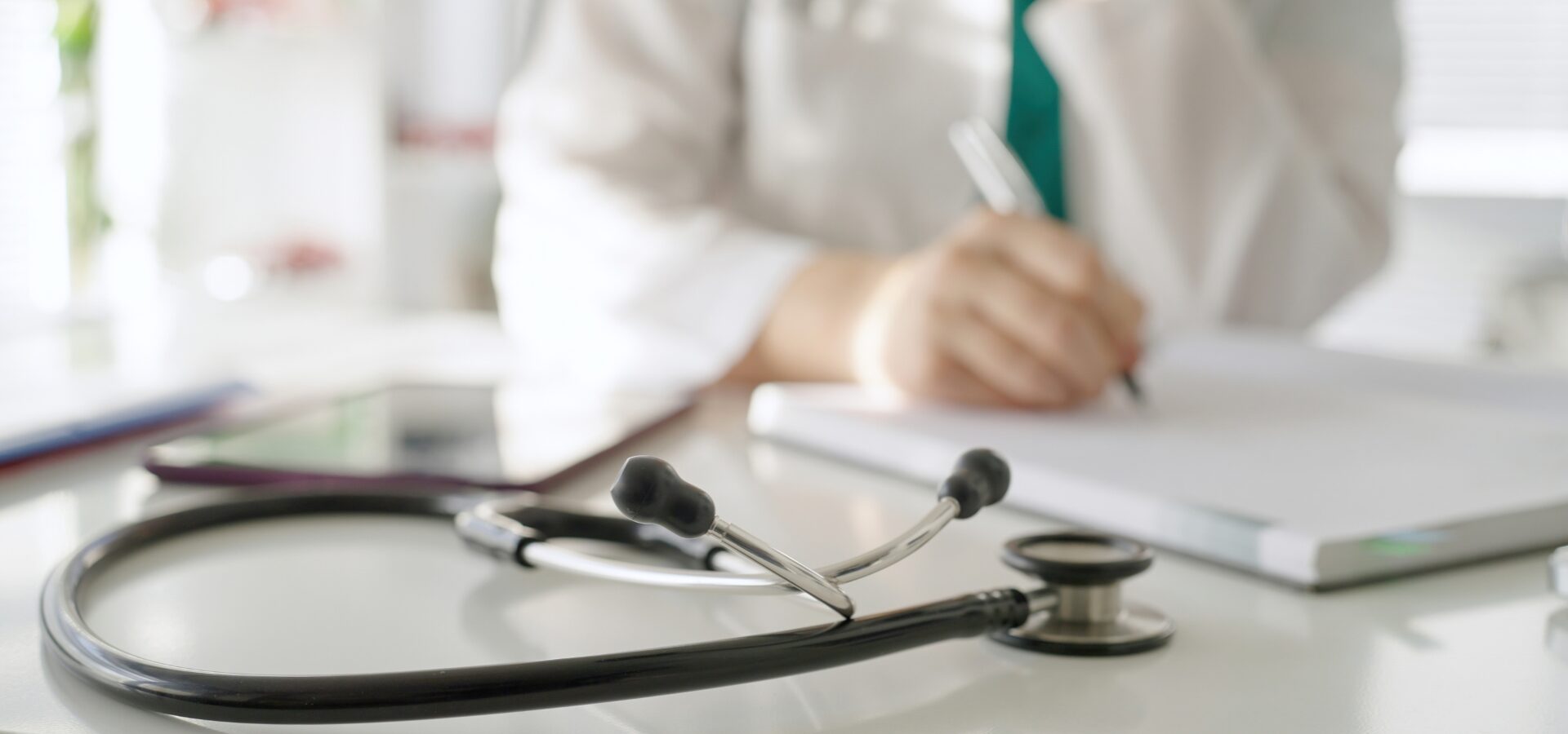 GP writing at desk, with stethoscope